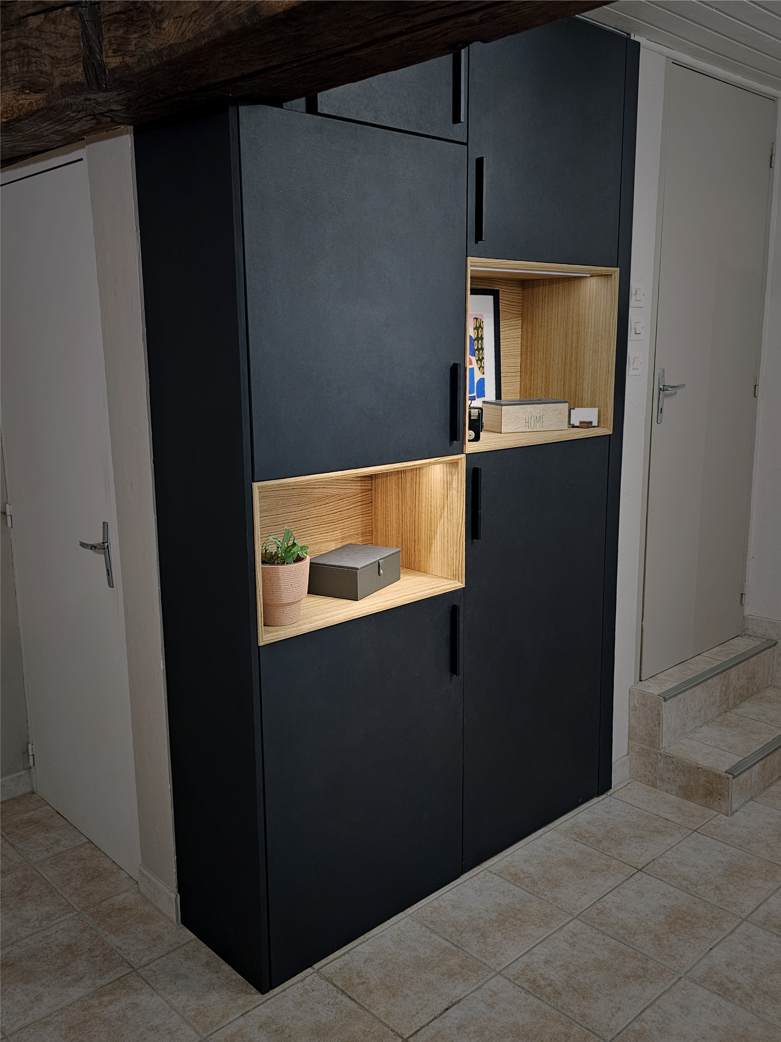 Meuble d'agencement noir mat avec niches en chêne éclairées, intégré sous poutres apparentes