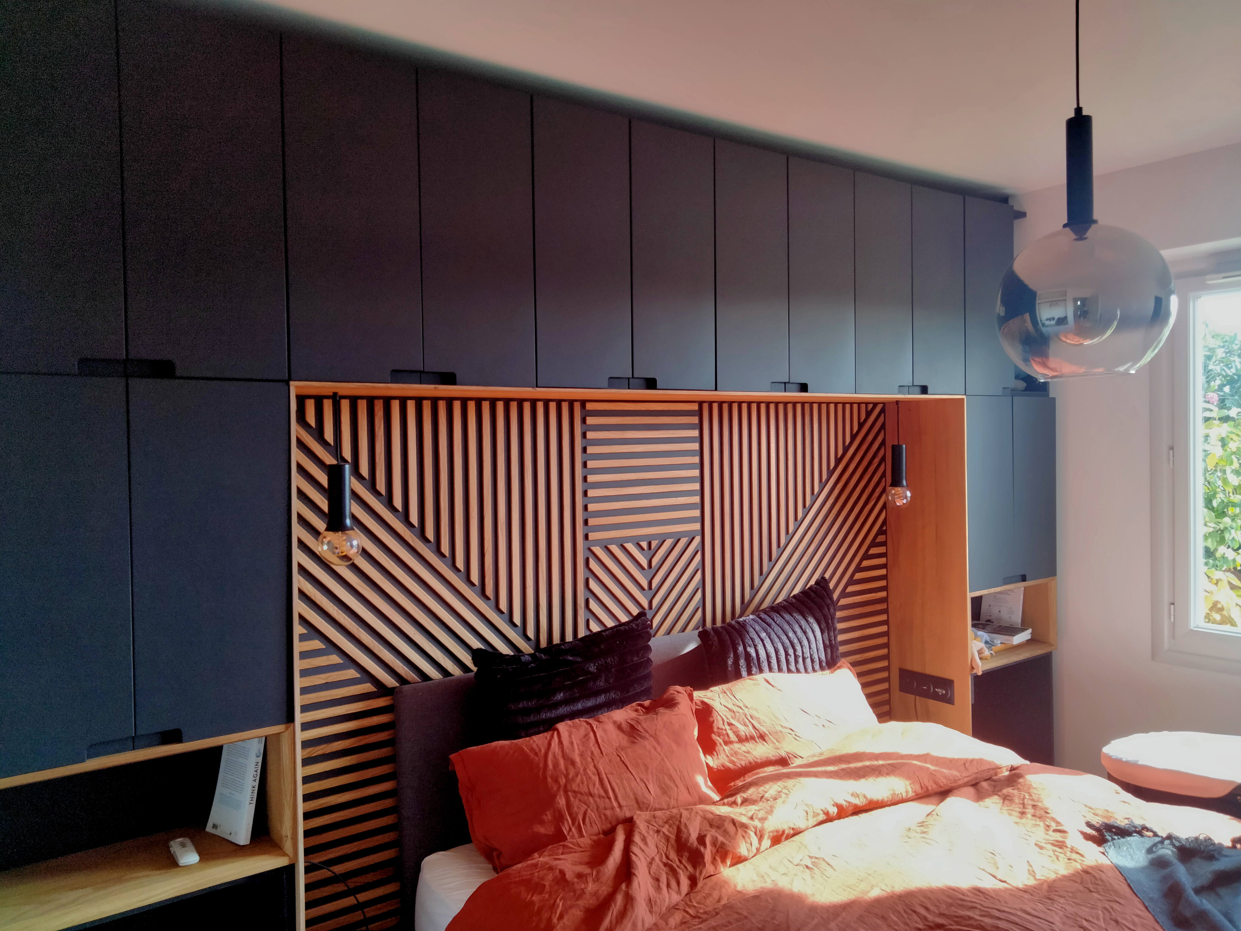 Chambre sur-mesure : tête de lit en lames de bois géométriques avec dressing noir mat toute hauteur et suspensions