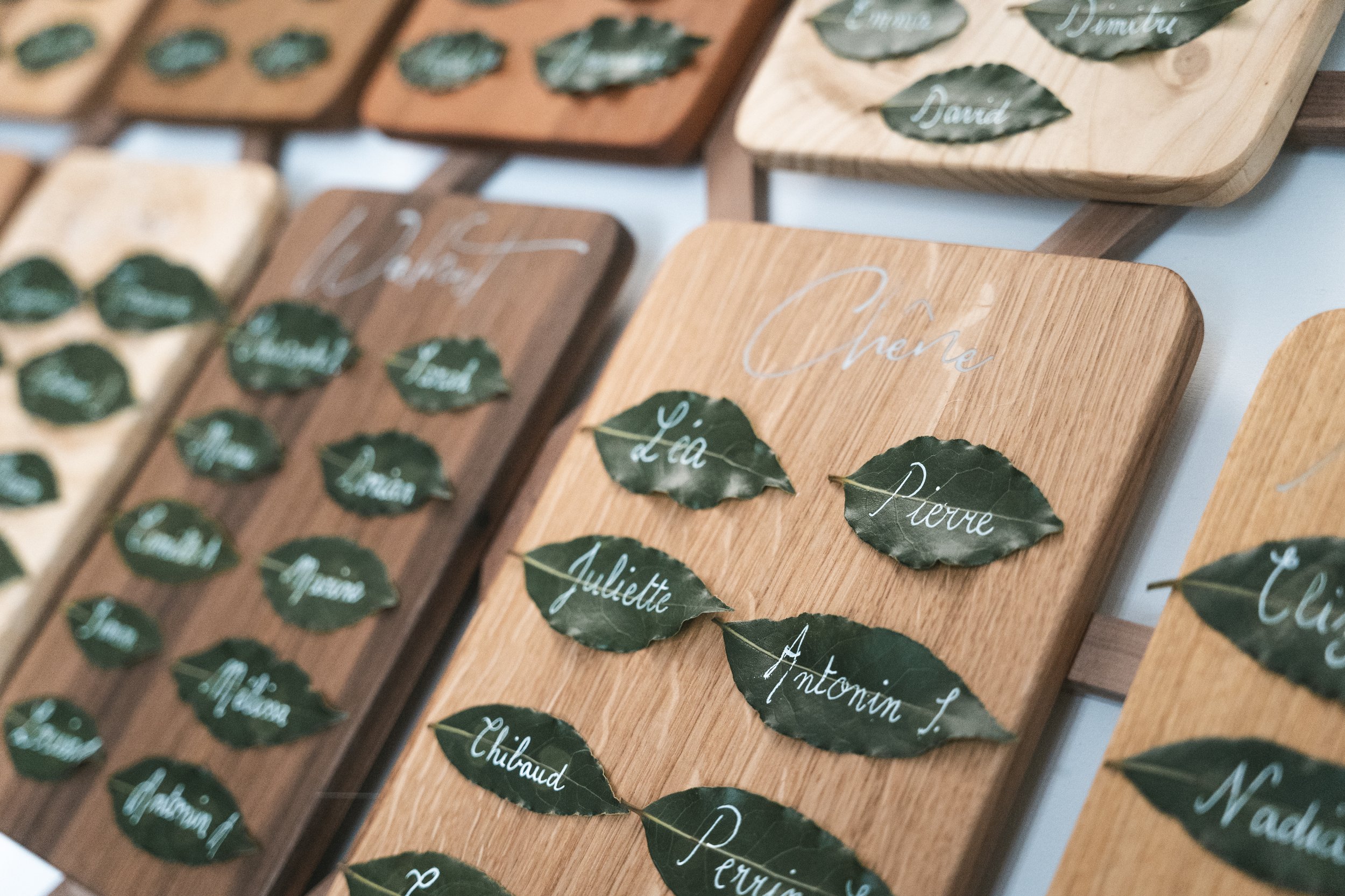 Détail plan de table de mariage avec planchettes en chêne et noms calligraphiés sur feuilles de laurier