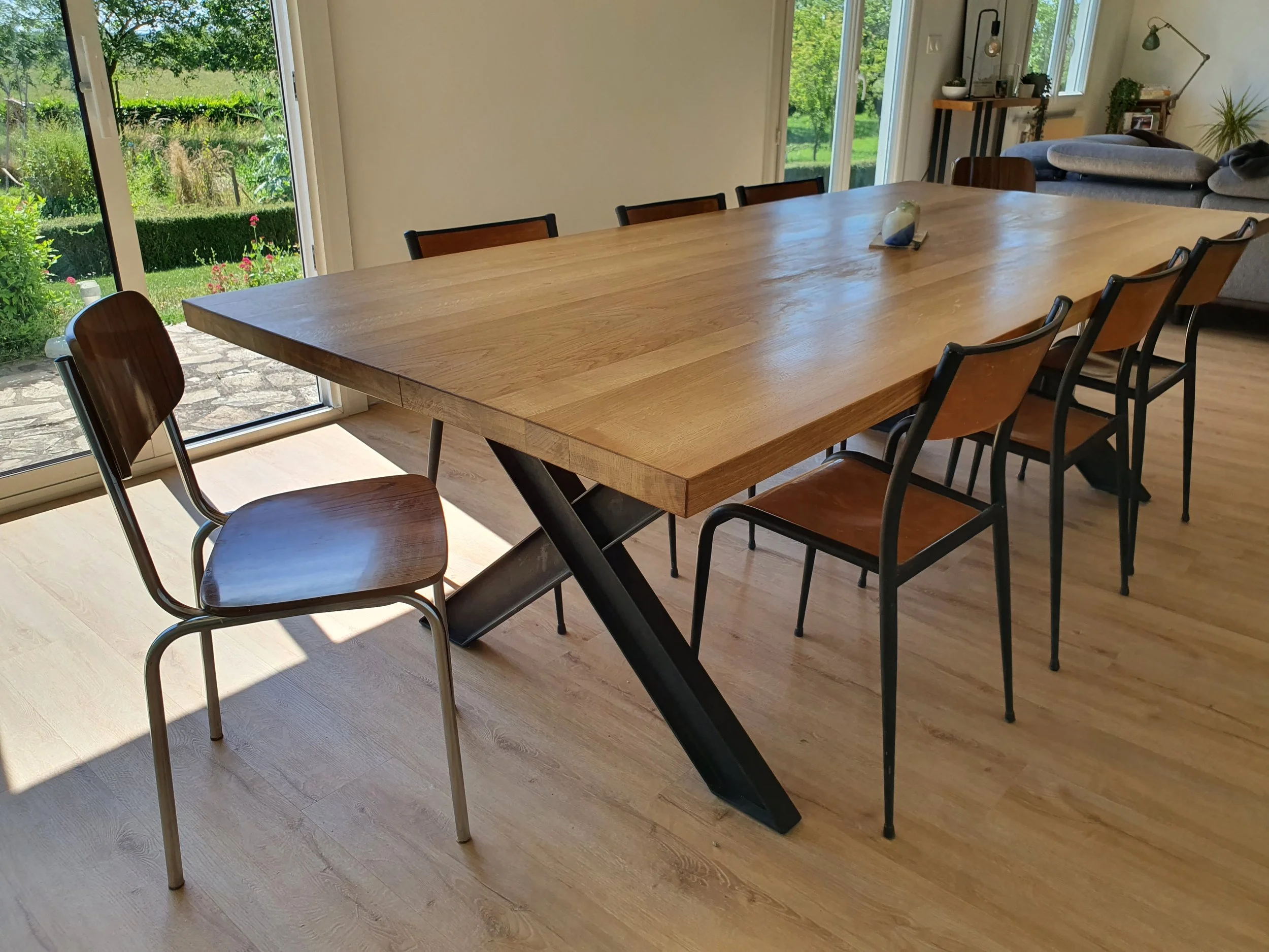 Table de salle à manger en chêne massif avec piètement acier en X, baignée de lumière naturelle